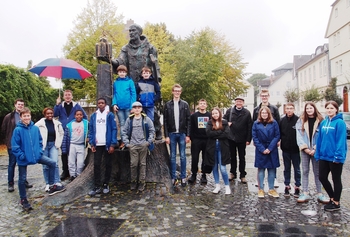 Fritzlar  Mit Bonifatius auf der gefällten Donar-Eiche: Die Messdienergruppe am Denkmal vor dem Fritzlaer Dom. Diakon Philipp Schöppner mit Schirm. 